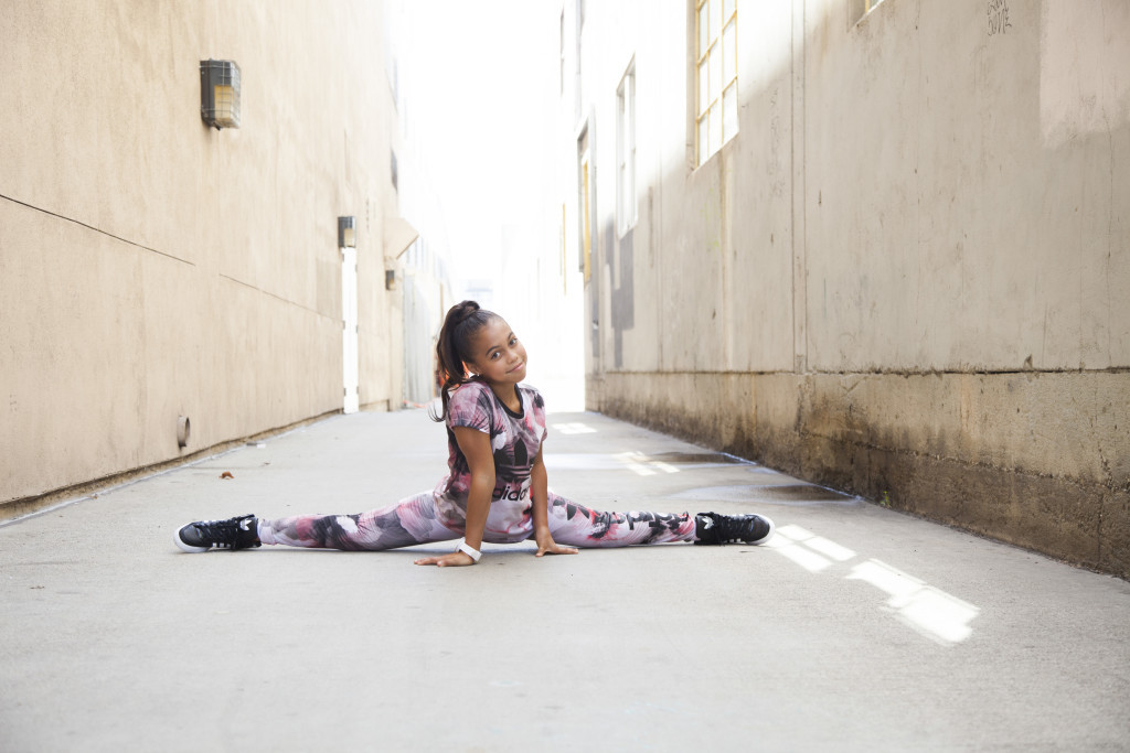 Asia Monet Ray doing the splits in an alleyway.