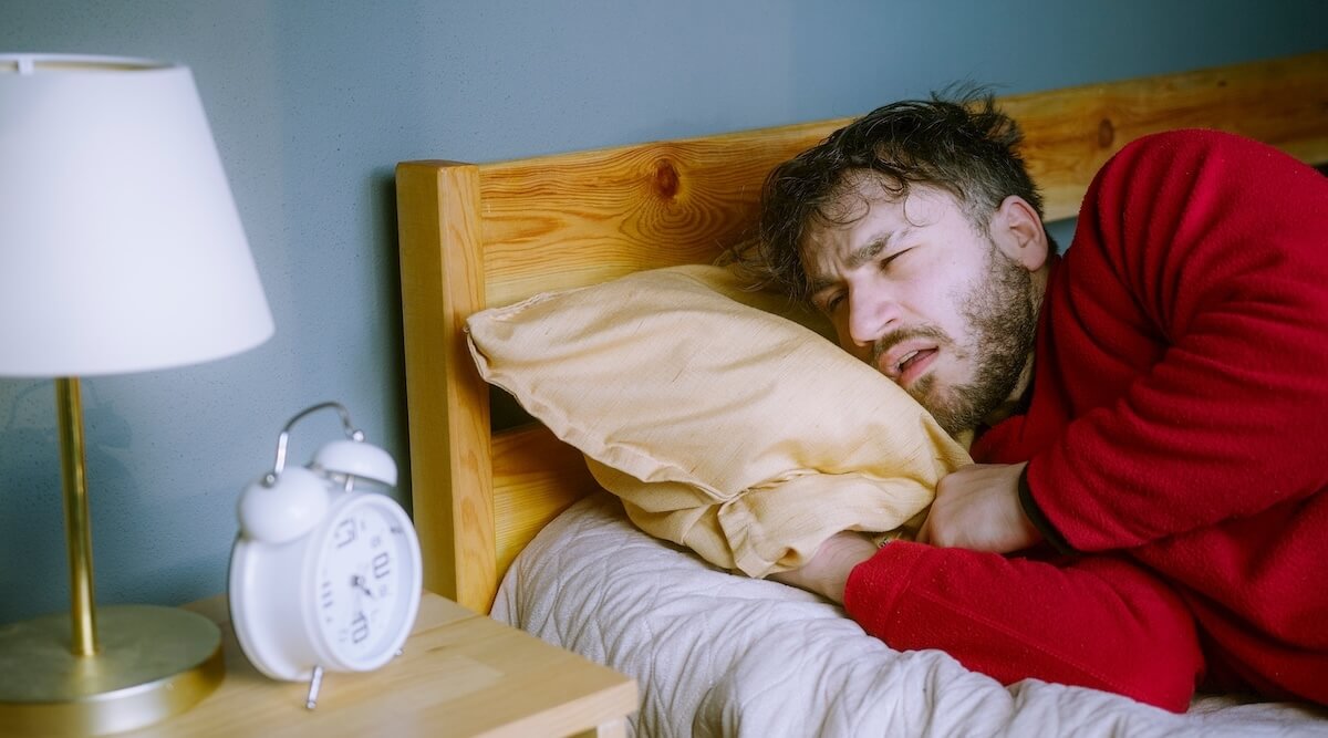 Shutterstock: Young man Struggling to Wake Up – Looking Snooze on Alarm Clock