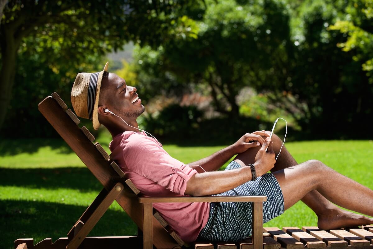 Shutterstock: Side portrait of young african guy sitting on chair and listening to music outdoors