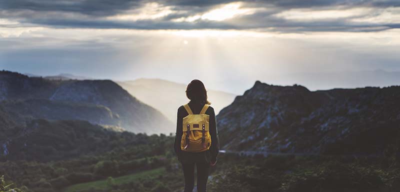 Girl with backpack on standing on the edge of a mountain top