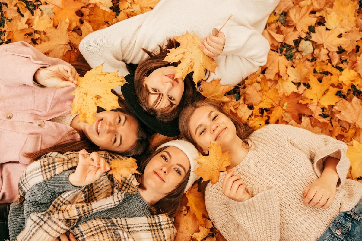 Shutterstock: Autumn portrait of Happy four young women students playing with leaves, smiling while lying on ground in park, top view