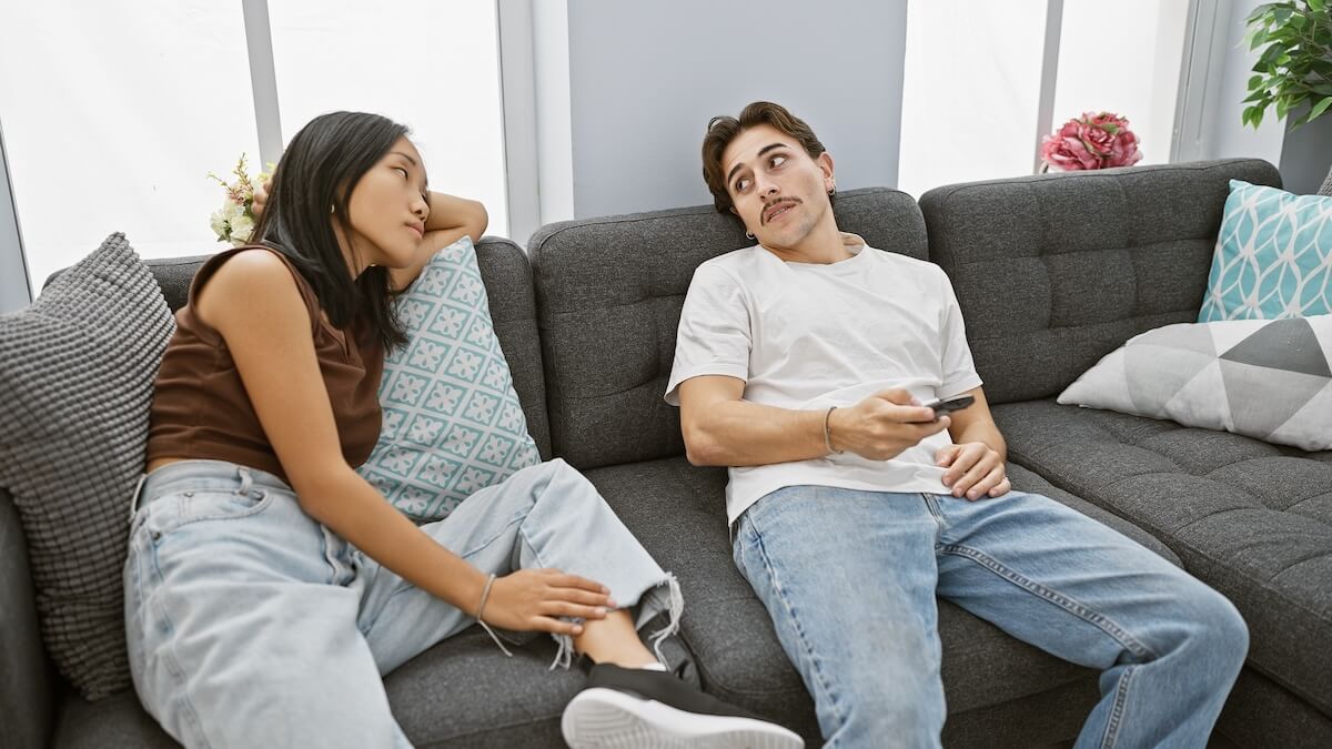 Shutterstock: Bored interracial couple, woman and man, lounging in a modern living room with a smartphone