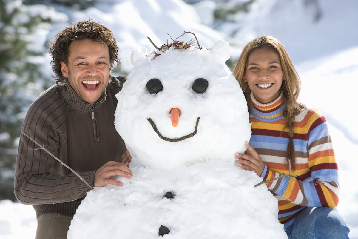 Shutterstock: Portrait of smiling couple building snowman on winter vacation