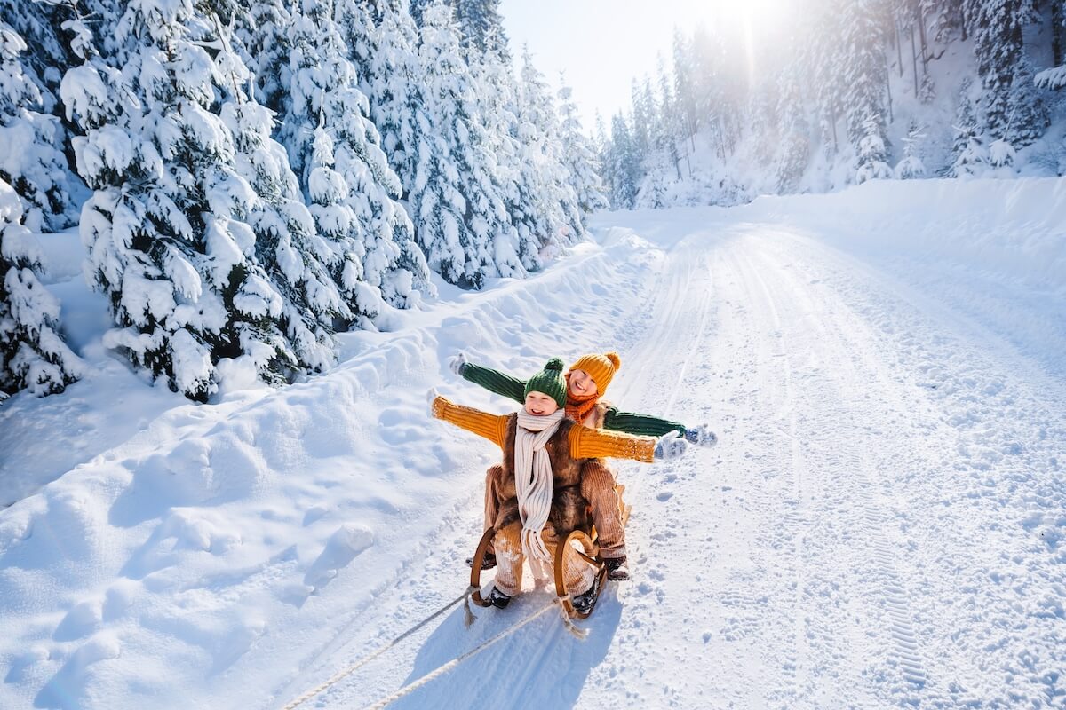 Shutterstock: Happy funny children ride wooden retro sleds on snowy road in mountains. Family on winter walk.