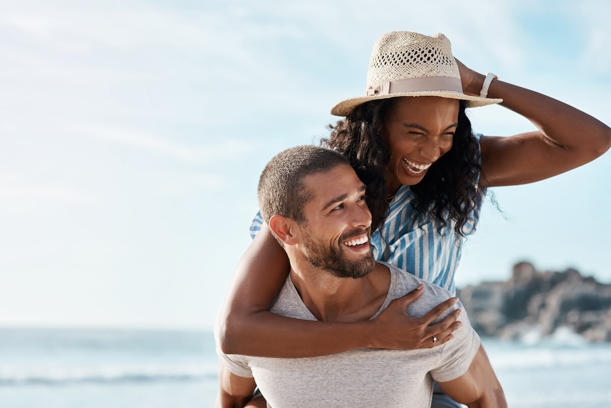 Unsplash: Happy couple, adventure at sea and piggy back with blue sky, mockup space and summer holiday travel to ocean. Romance, man and woman at beach with happiness on date and vacation together in Cancun.