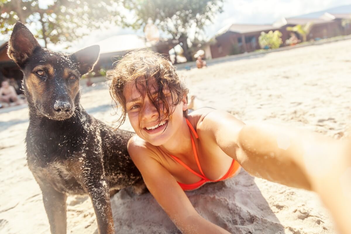 Shutterstock: pretty young woman doing selfie with her dog on the beach at sunset