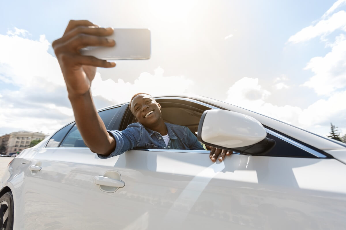 Shutterstock: Emotional afro american guy taking selfie, shooting story for his friends and followers on social media while sitting inside nice white car, using mobile phone, selective focus on hand with cellphone