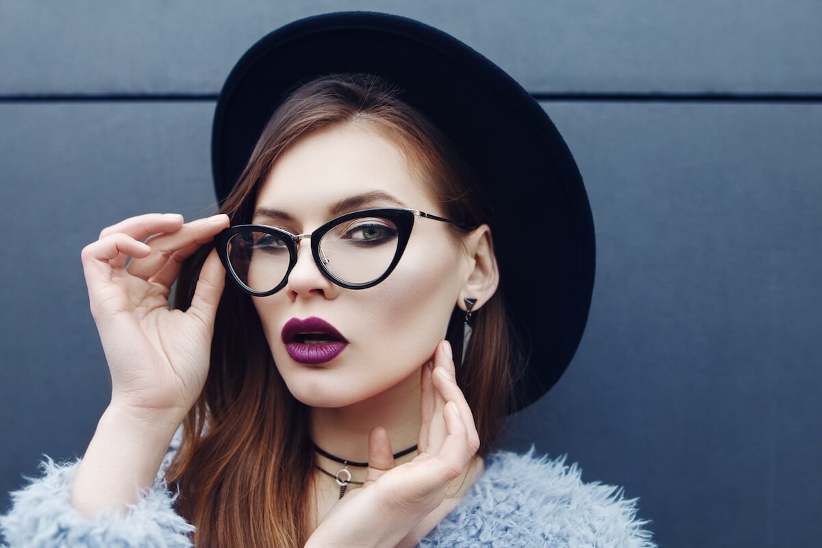 Shutterstock: Young beautiful fashionable woman with long hair, trendy makeup. Model looking at camera, wearing stylish eyeglasses, fake fur coat, hat, accessories. Female fashion, beauty concept. Outdoor. Close up