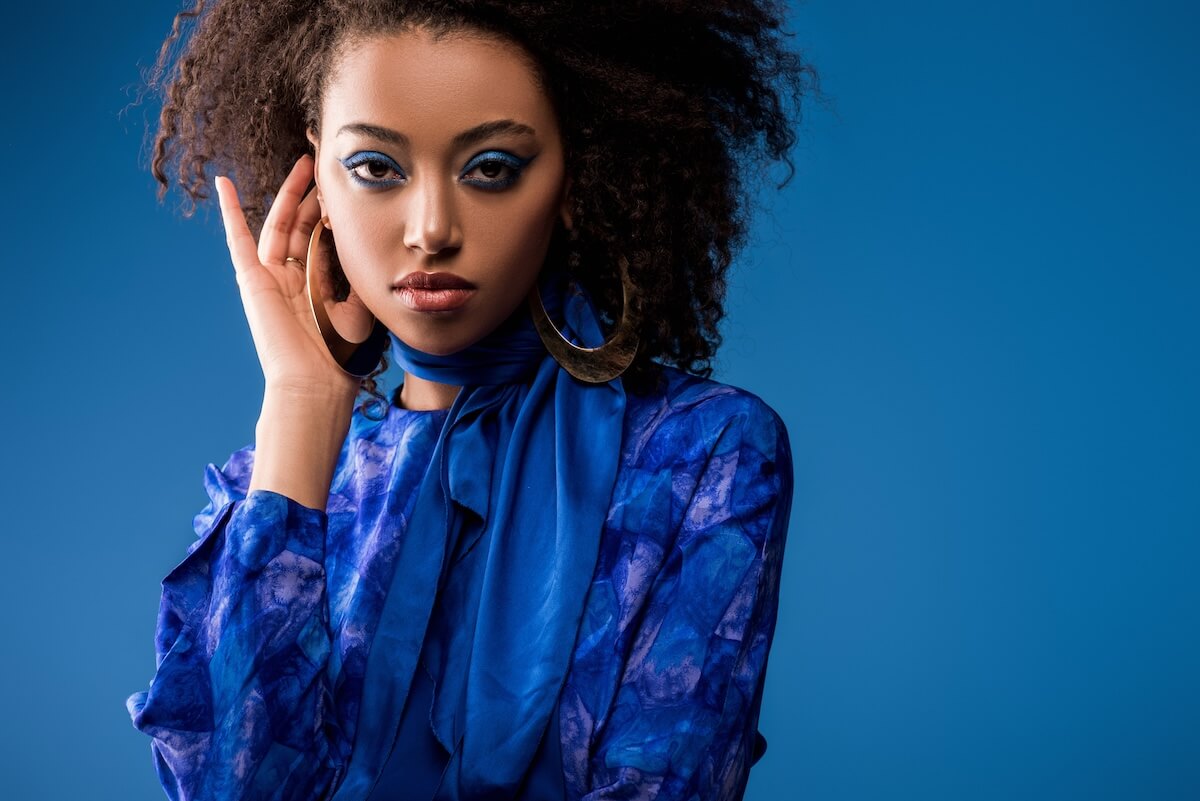 Shutterstock: attractive african american woman in dress and earrings looking at camera isolated on blue