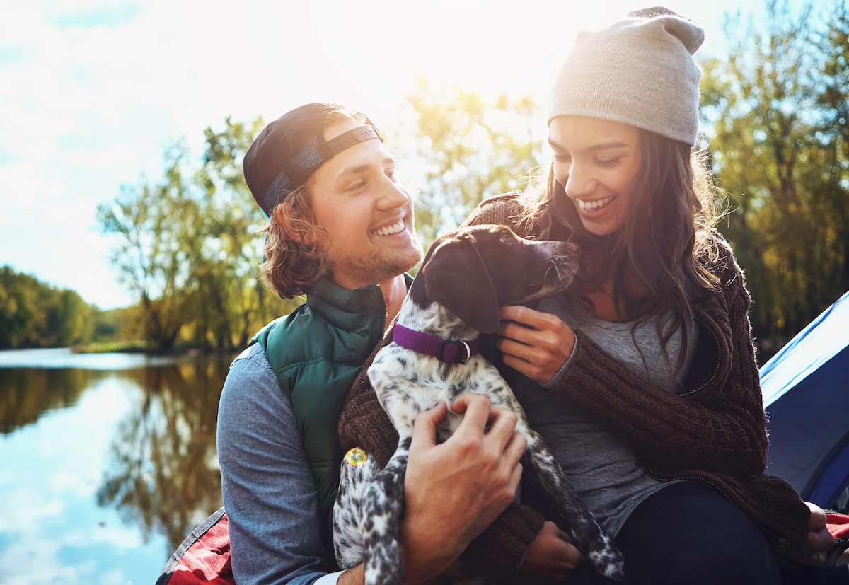 Shutterstock: Couple, camping and lake in nature with dog for freedom, adventure travel with sustainability. Man, woman and pet in countryside by water for relax on vacation, happiness for holiday environment