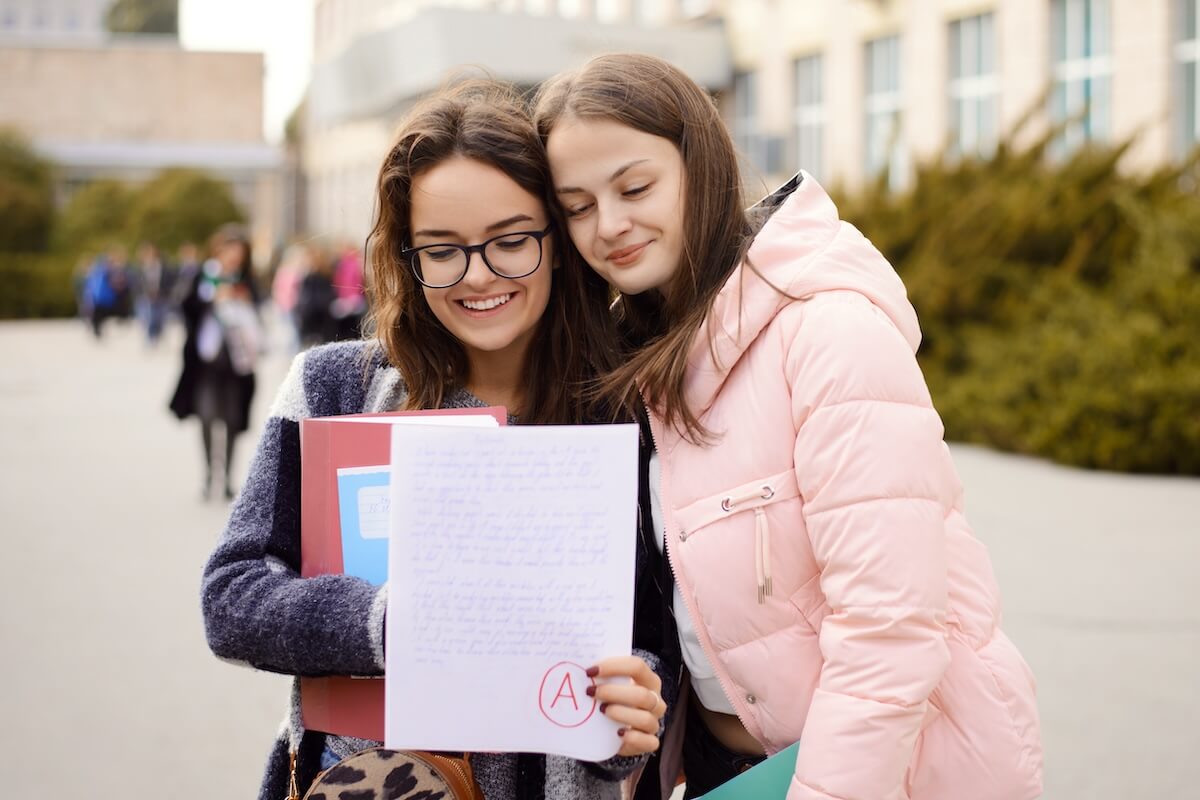Shutterstock: Successful passing of important examination. Happy female student with a friend looking to the test sheet with excellent A grade result