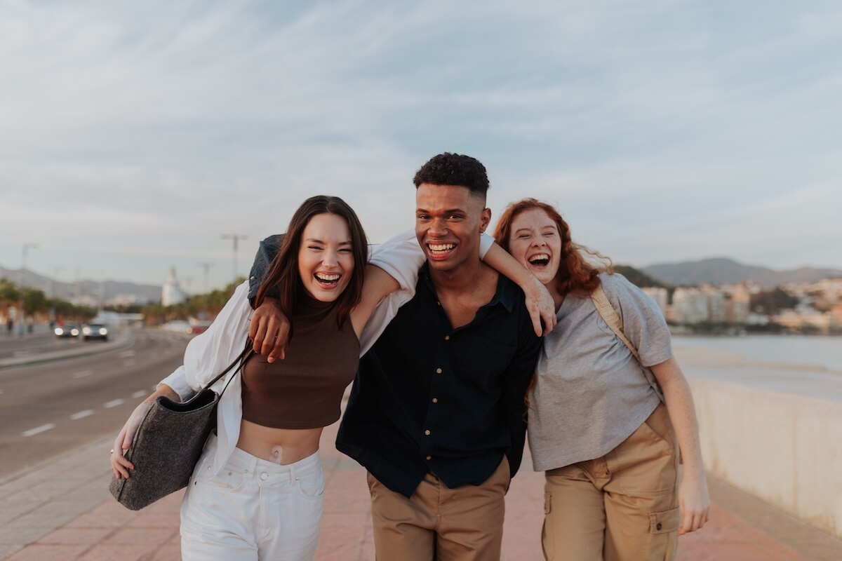Shutterstock: Blissful friends laughing and having fun in the waterfront. Group of three happy friends taking a stroll along the promenade. Multicultural friends enjoying a weekend getaway in a coastal town.