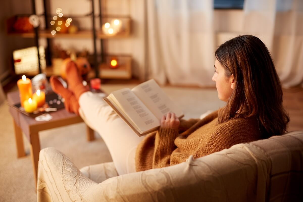 Shutterstock: halloween, holidays and leisure concept - young woman reading book and resting her feet on table at cozy home