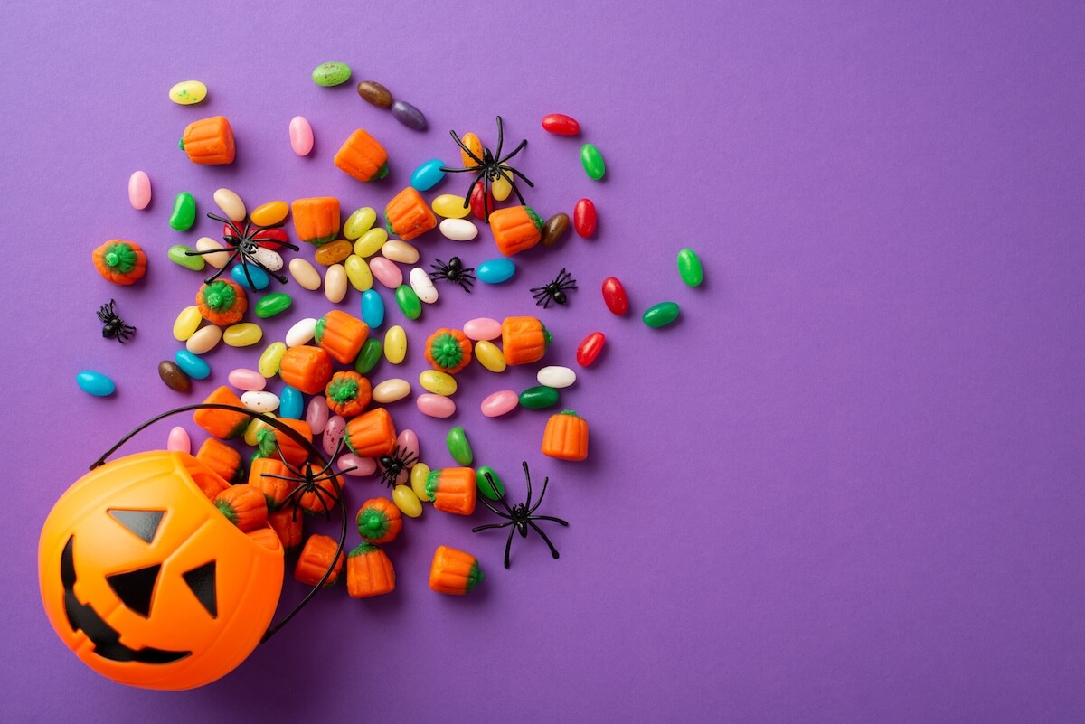Shutterstock: Top view photo of halloween decorations pumpkin basket with candies and spiders on isolated violet background