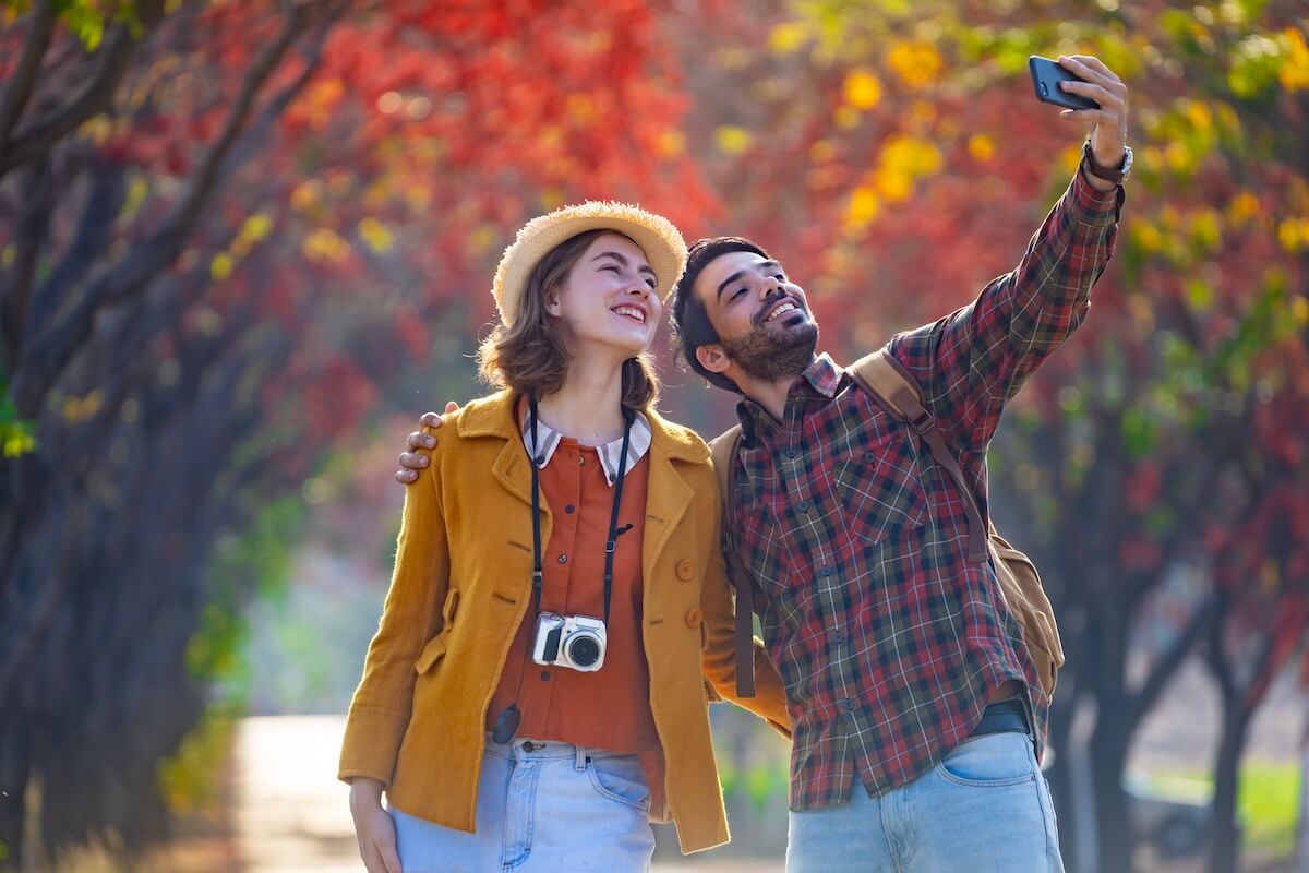 Shutterstock: Happy caucasian couple are walking together in the public park during autumn with maple and beech tree while taking selfie for fall color travel destination and family happiness