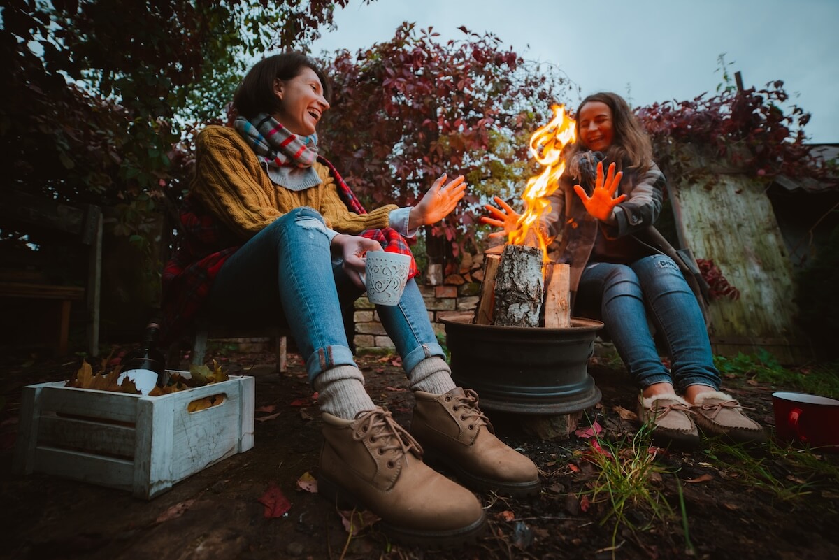 Shutterstock: two friends relax comfortably and drink wine on an autumn evening in the open air by the fire in the backyard. The concept of autumn, friendship. top view of the legs