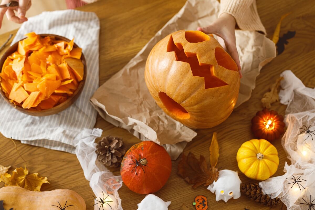 Shutterstock: Woman carving halloween pumpkin on table with ghosts and spiders. Carving jack o lantern, halloween preparation. Making halloween decorations