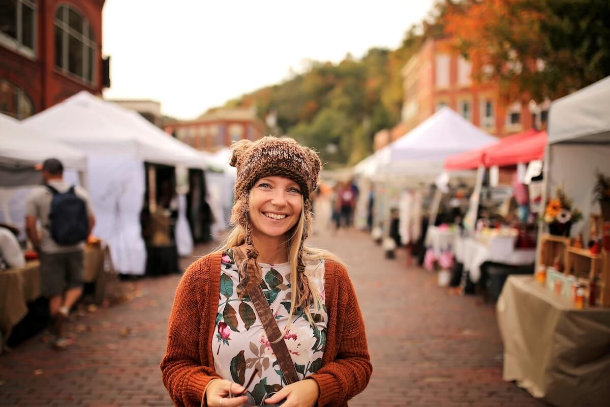 Shutterstock: A happy women wearing a hand knit fox winter hat is smiling as she shops outside at a small town fall festival market.