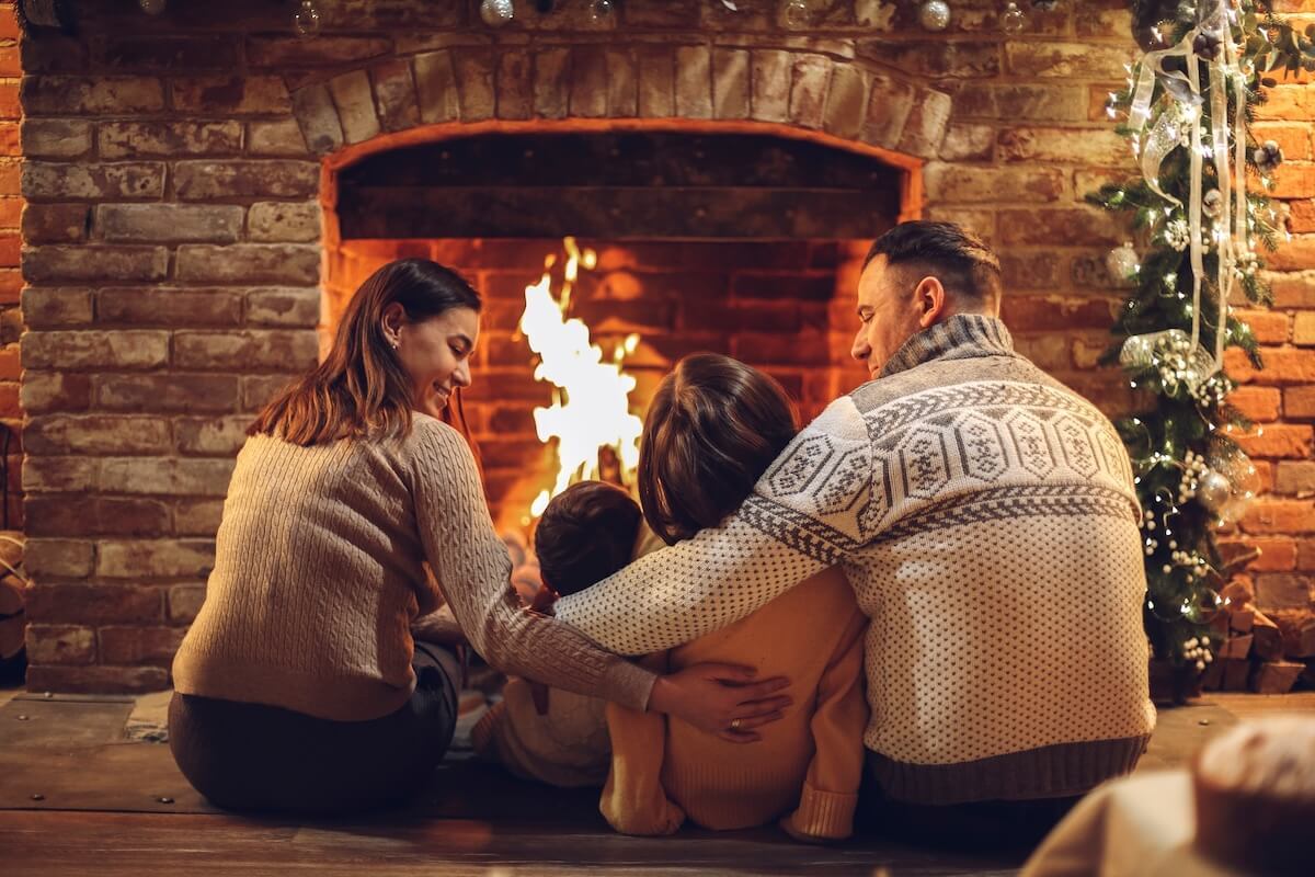 Shutterstock: Happy young family parents with two small kids gathering around brick fireplace in cozy and warm country house during Christmas holidays in winter. Father, mother ad children sitting by fire at home