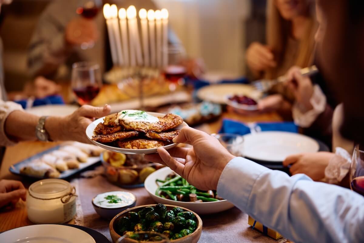 Shutterstock: Close up of Jewish people passing latkes during traditional Hanukkah dinner at dining table.