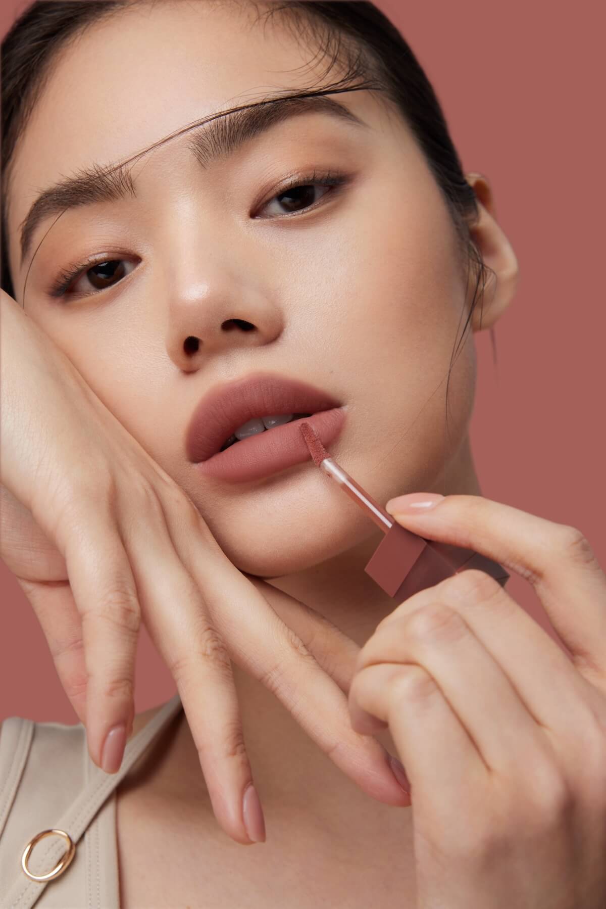 Shutterstock: Elegant Close-Up of a Woman Applying Matte Nude Lipstick - Beauty and Makeup Concept on a Warm, Minimalist Background.