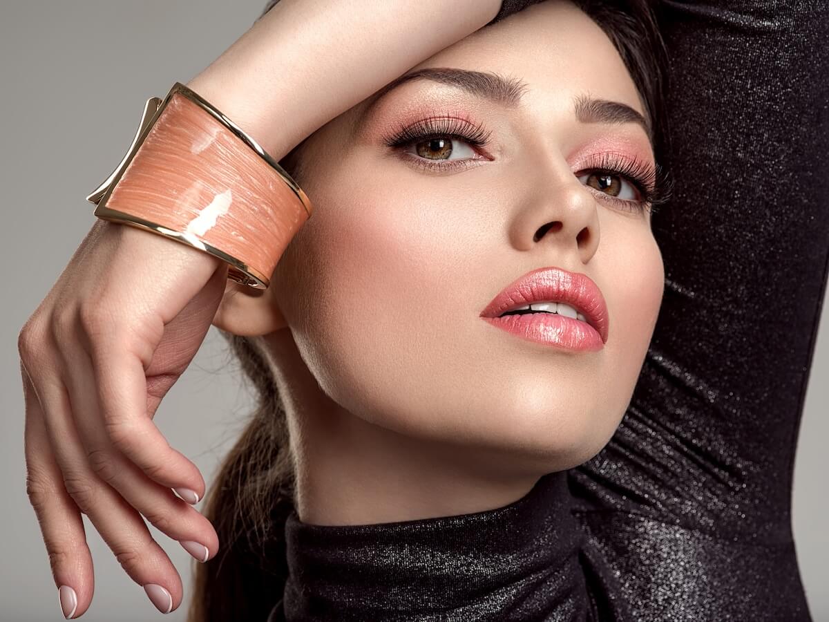 Shutterstock: Beautiful young fashion woman with living coral lipstick. Attractive white girl wears luxury jewelry. Glamour fashion model with bright make-up, at studio. Stylish fashionable concept. Bracelet.