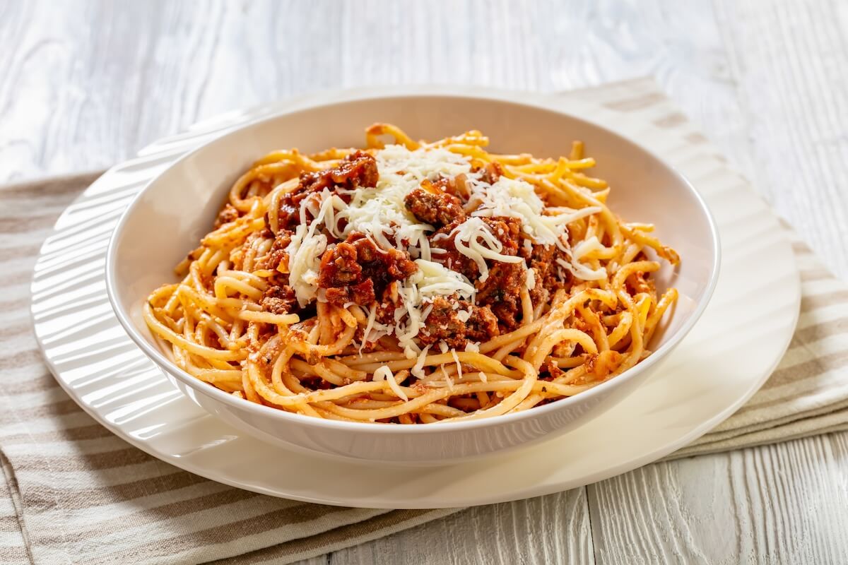 Shutterstock: spaghetti al ragu alla Bolognese topped with shredded cheese in white bowl om white wood table, horizontal view from above