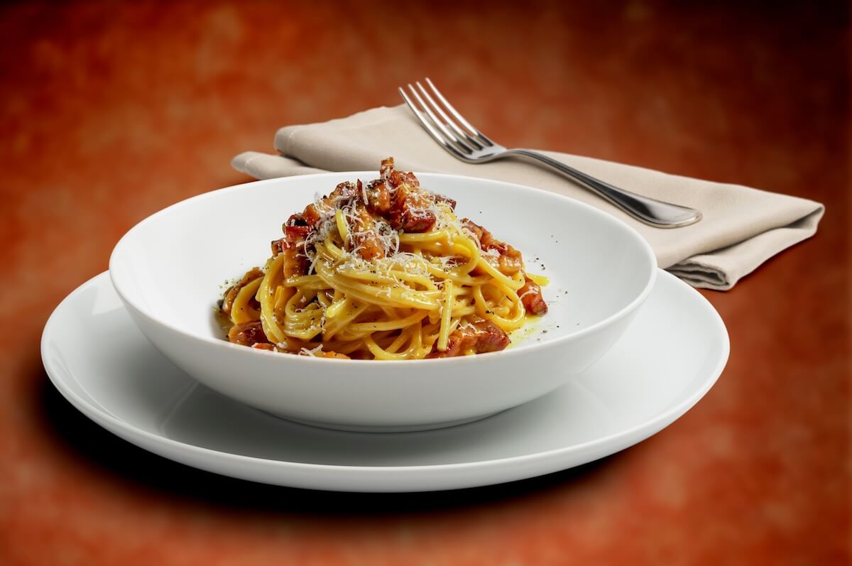 Shutterstock: Bowl with spaghetti alla carbonara with napkin and fork solated on a speckled background