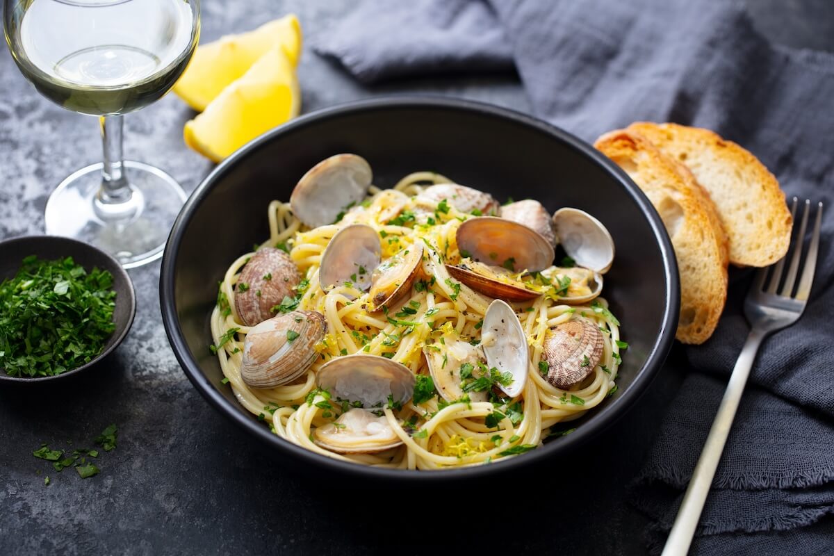 Shutterstock: Spaghetti alle vongole, seafood pasta with clams in a black bowl and glass of white wine. Dark background. Close up.
