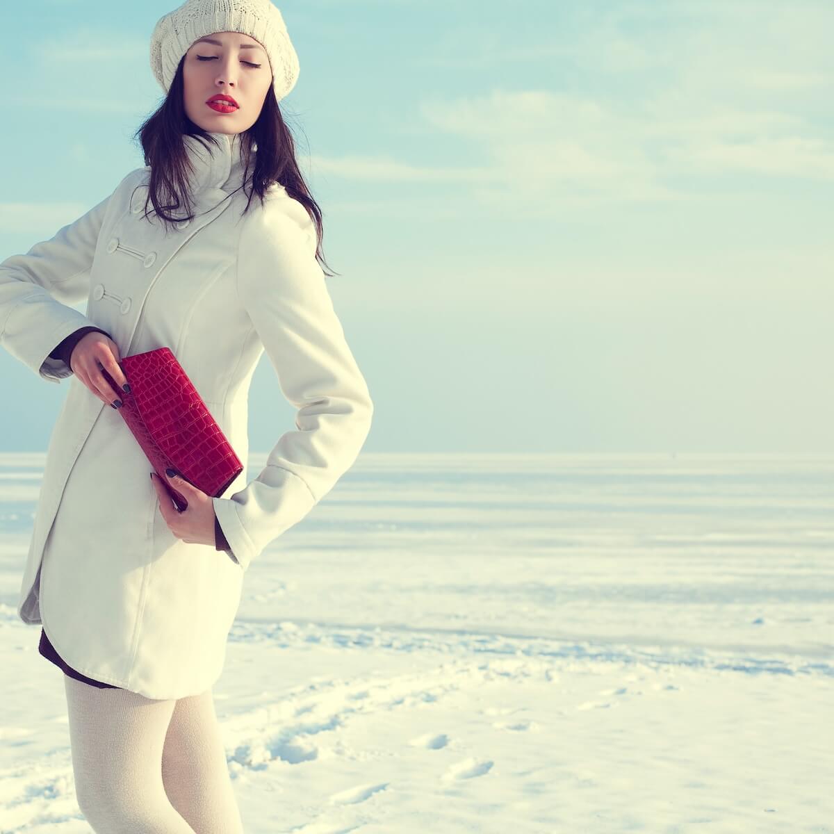 Shutterstock: Portrait of a fashionable model in white coat and beret holding red leather clutch and posing at the winter seaside. Sunny weather. French vintage (retro) style. Copy-space. Outdoor shot.