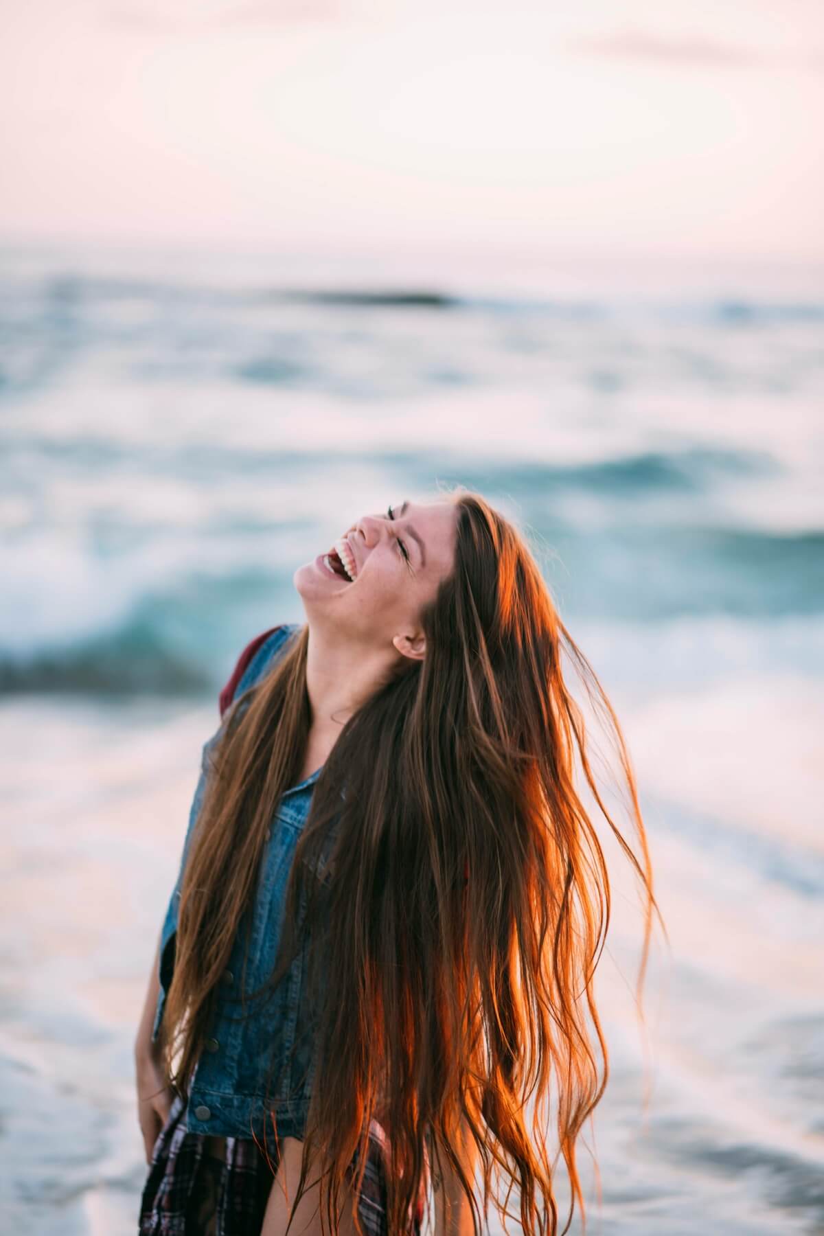 Unsplash: Woman with long hair laughing at beach by Jenna Anderson