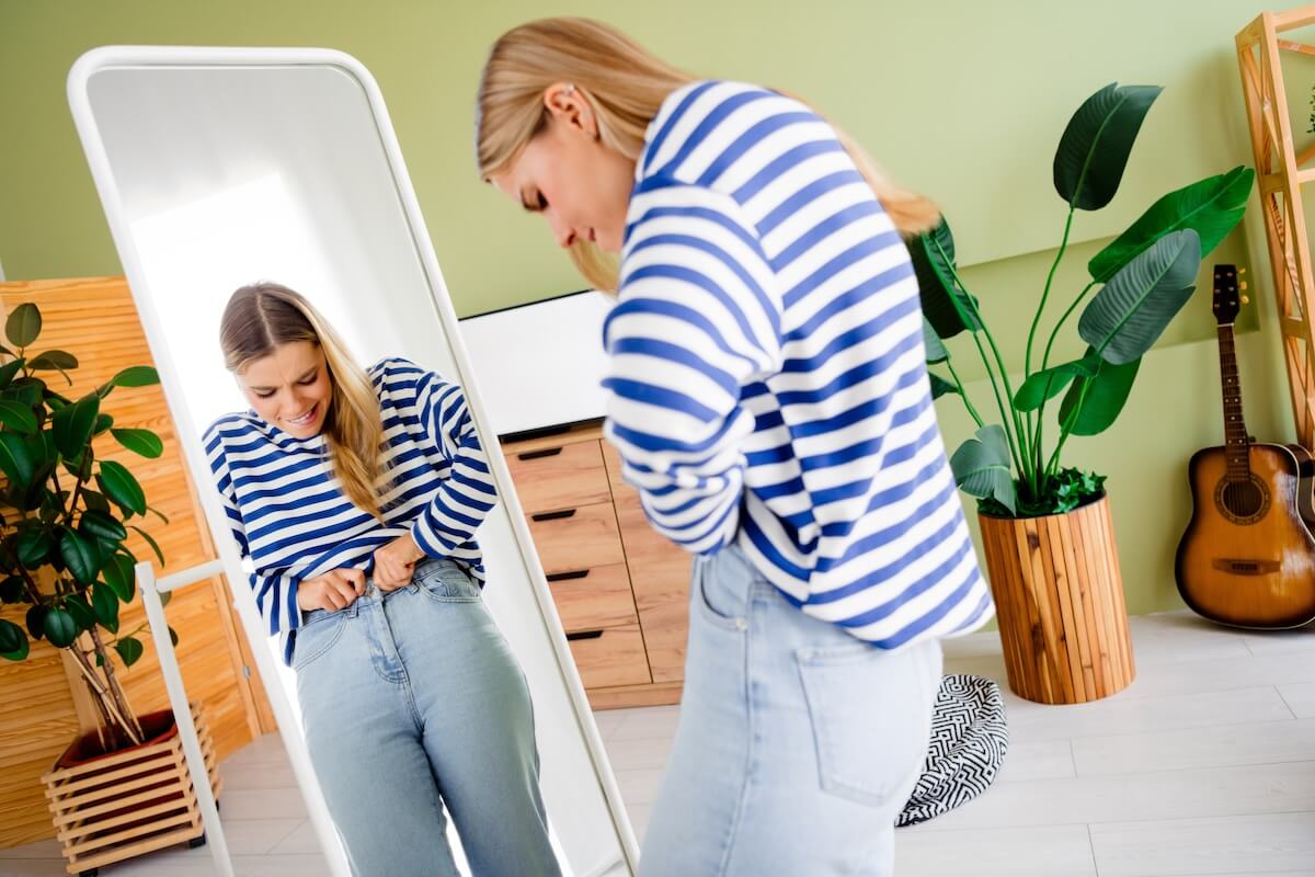 Shutterstock: Photo of nice blonde young girl look mirror unhappy try on button jeans wear striped clothes enjoy modern cozy interior flat indoors