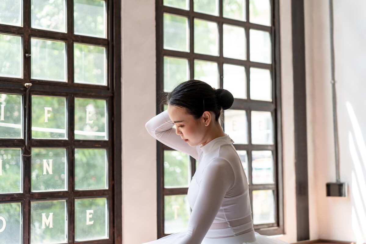 Shutterstock: Asian girl ballet dancer preparing fixing her hair into a bun during ballet class. ballerina adjusting her hair