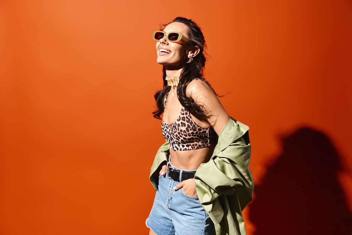 Shutterstock: A fashionable woman wearing a leopard print top and denim shorts, exuding confidence and style on an orange background.