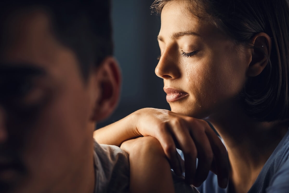Shutterstock: Sad woman crying with eyes closed while leaning on boyfriend's shoulder.