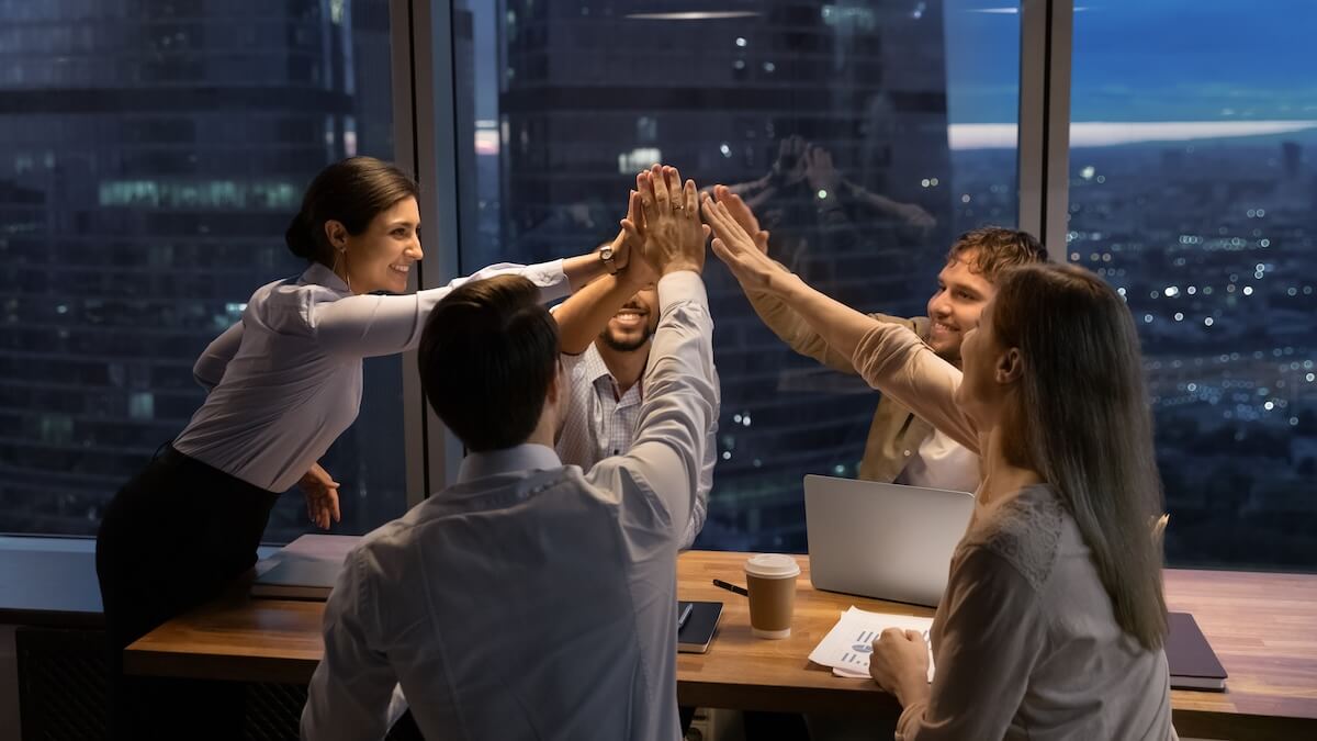 Shutterstock: Motivated multinational team raise high fives on briefing after finding problem solution as successful brainstorm result. Happy workers unite hands above conference desk celebrate common achievement