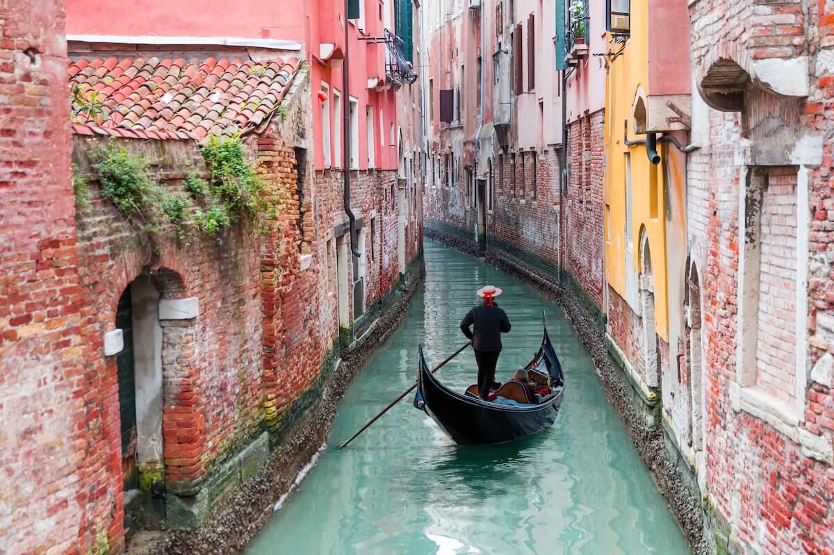 Shutterstock: Venetian gondolier punting gondola through green canal waters of Venice, Italy