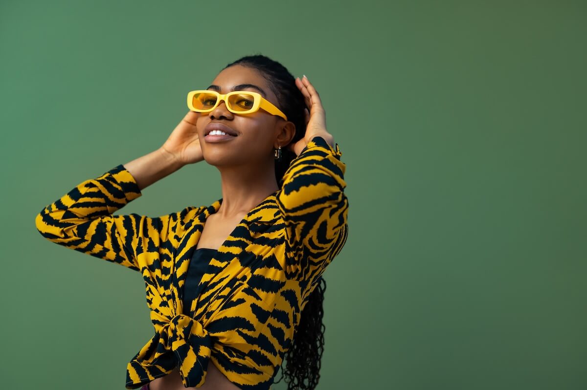 Shutterstock: Fashionable happy smiling Black woman wearing trendy yellow rectangle sunglasses, animal, tiger print blouse, posing on green background. Copy, empty space for text