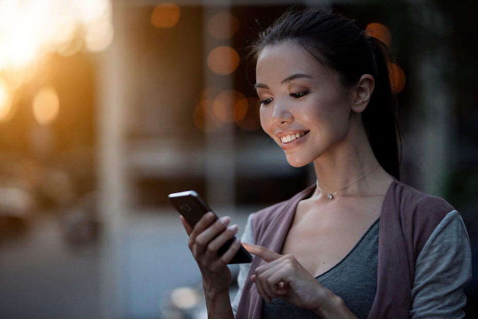 Shutterstock: Woman smiling outside looking at phone and touching screen