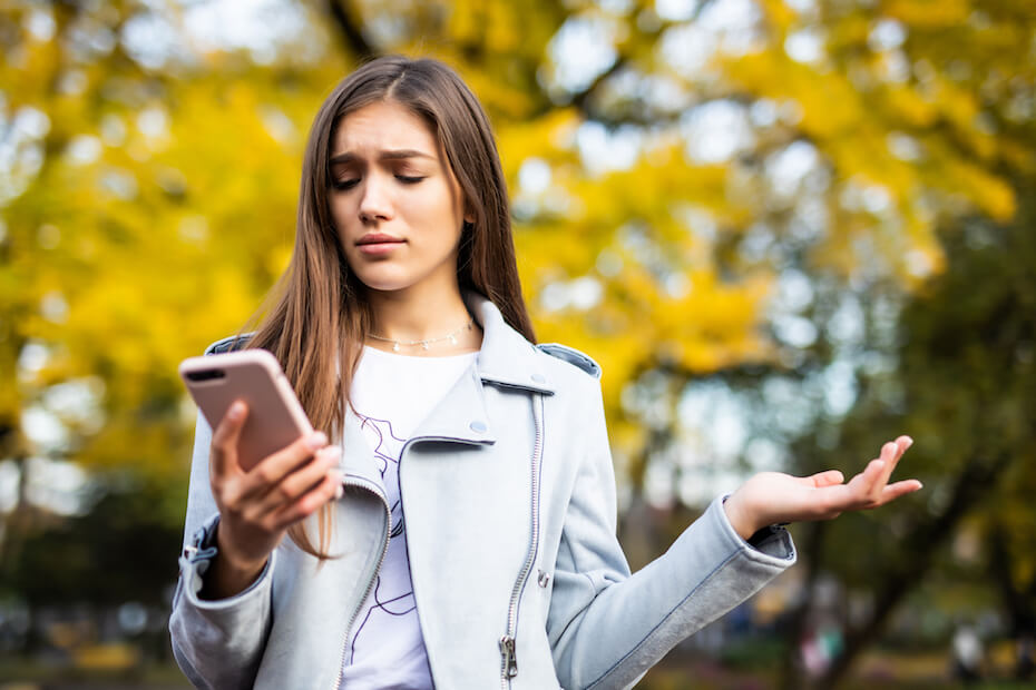 Shutterstock: Woman outside looking at phone annoyed outside