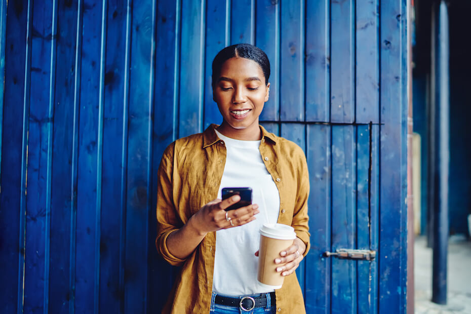 Shutterstock: Woman smiling looking at phone texting holding coffee