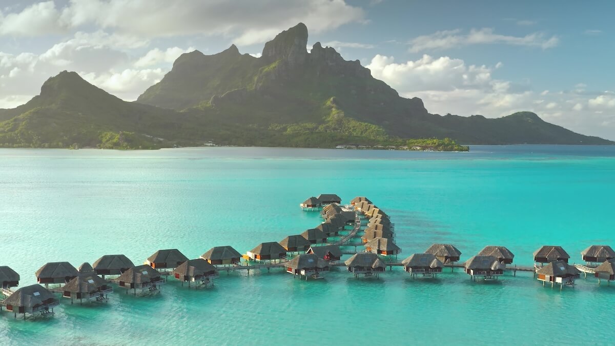 Shutterstock: Aerial view overwater bungalows forming line towards mount Otemanu on tropical exotic Bora Bora island, with its turquoise lagoon and lush vegetation. Luxury travel vacation resort in coral reef ocean