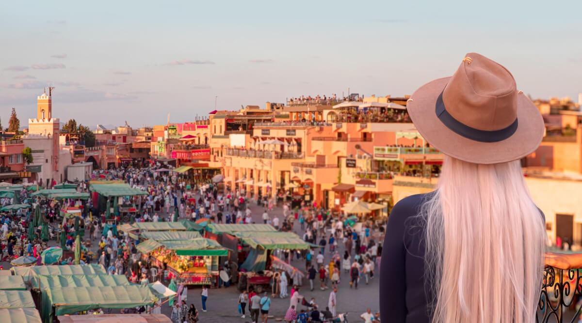 Shutterstock: A beautiful blondie young woman in a beige hat watches people in the Jemma el Fnaa or Djemma el Fna famous square in Marrakesh, Morocco