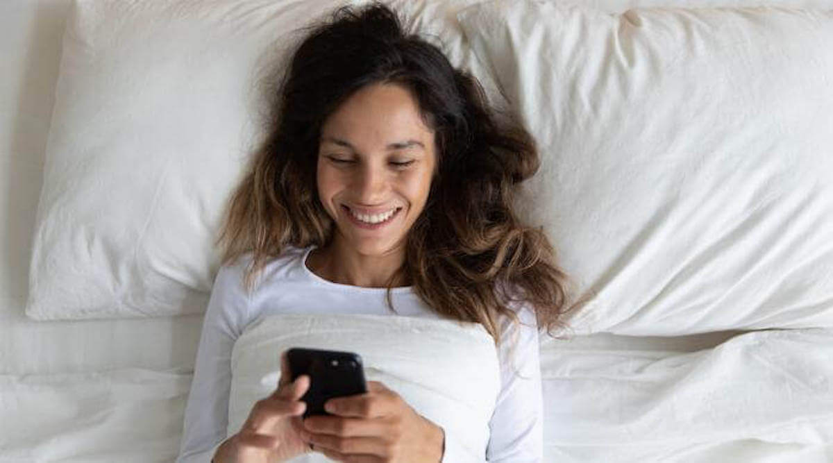 Shutterstock: Woman happily texting on phone in bed smiling