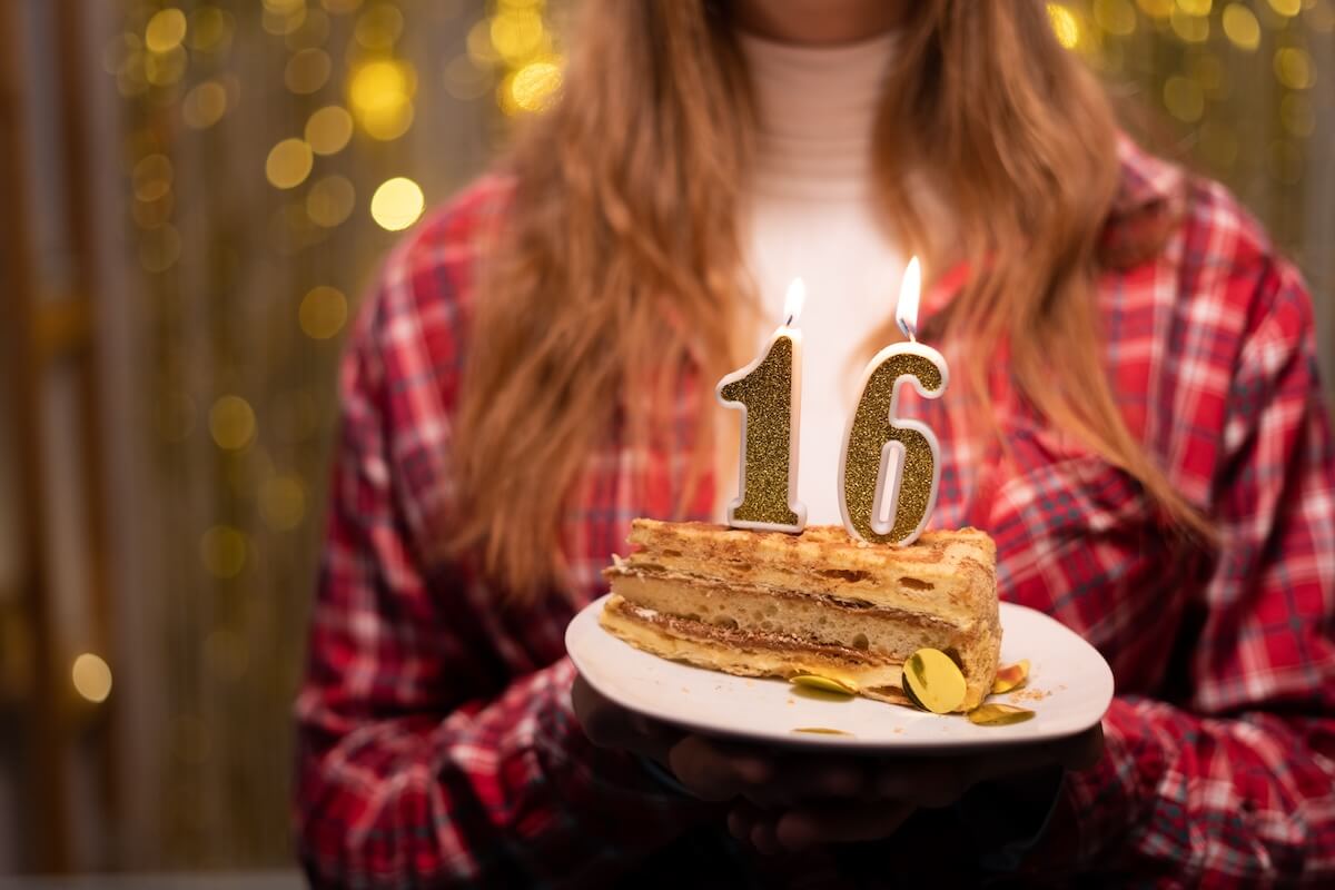 Shutterstock: Young woman holding plate with tasty birthday cake with 16 number candle against defocused lights. Copy space