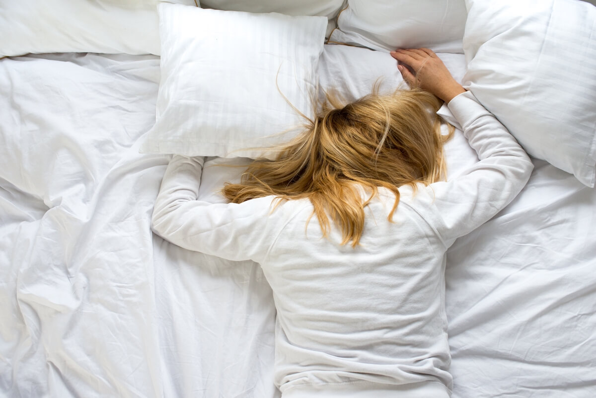 Shutterstock: A woman covers her face with a pillow. The woman lies tired on a white bed. Oversleep, not getting enough sleep concept. Young beautiful blonde woman lying in bed. Early wake up concept