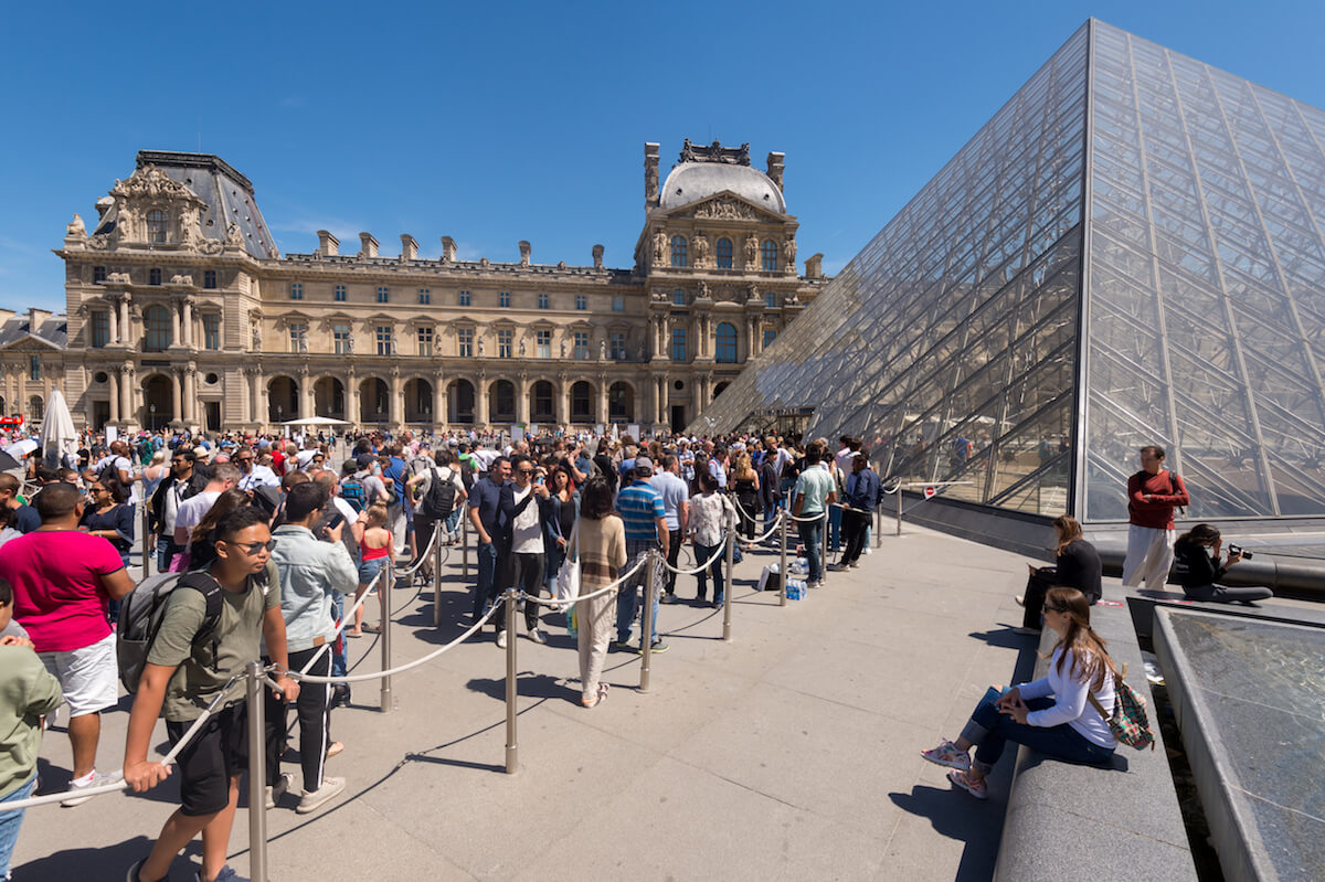 Shutterstock: Paris, France - 23 June 2018: Tourists waiting in line in front of the entrance to the Louvre museum