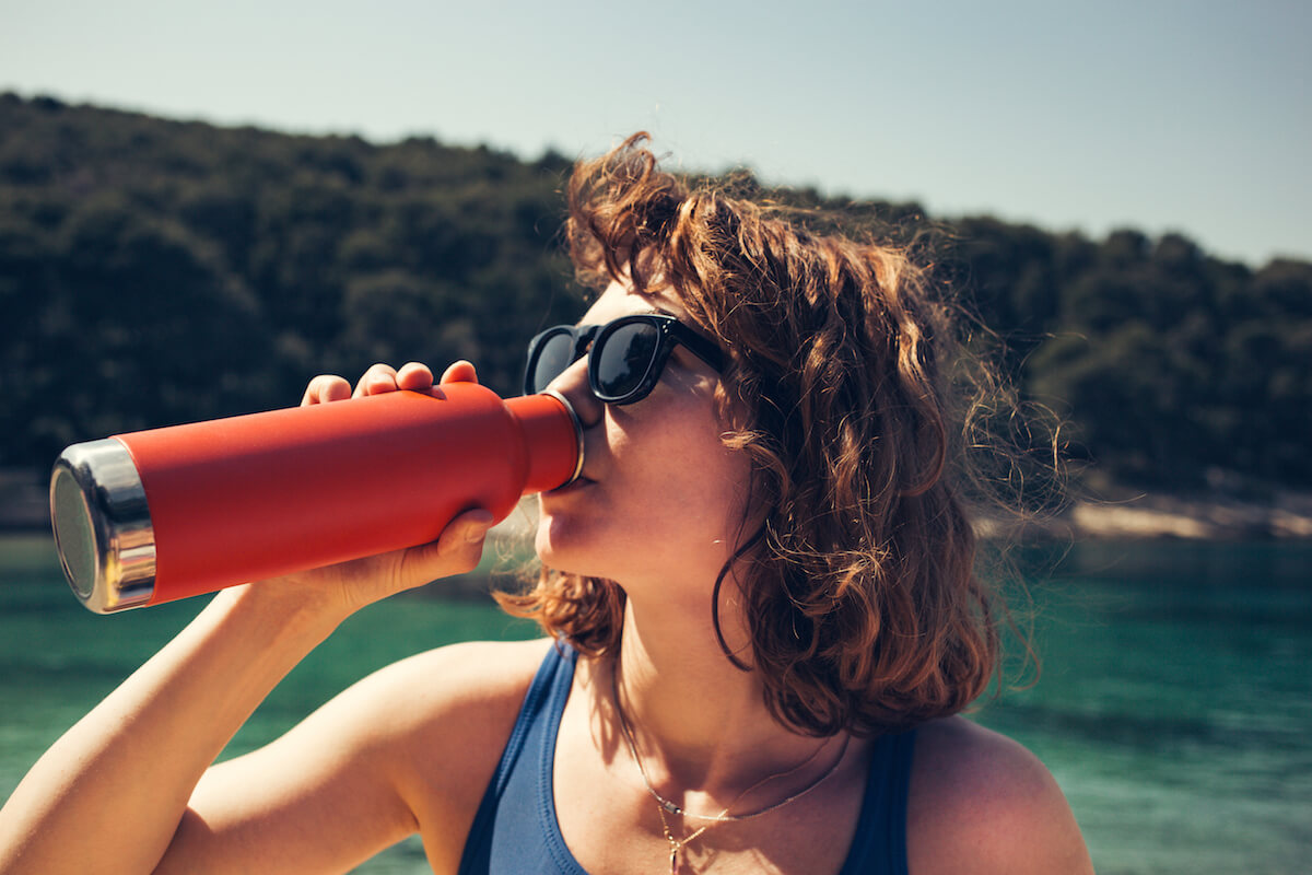 Shutterstock: A beautiful girl drinking from a steel water bottle at the beach