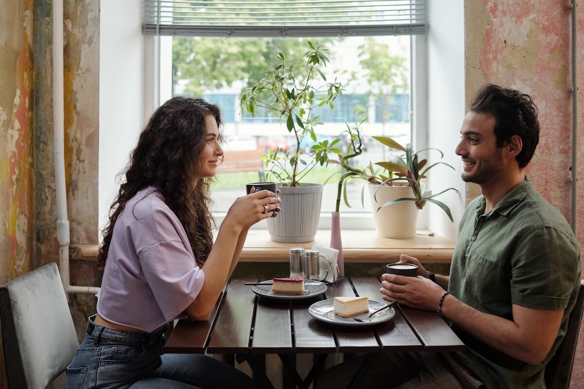 Shutterstock Young woman and her smiling boyfriend with cups of coffee sitting by table in front of one another and chatting