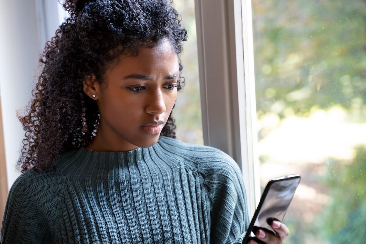 Shutterstock: African American female stares outside her window looking cellphone.